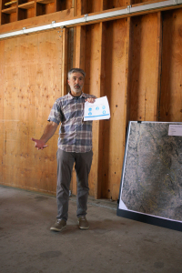 a man in a plaid shirt holds a chart and explains something inside a barn building