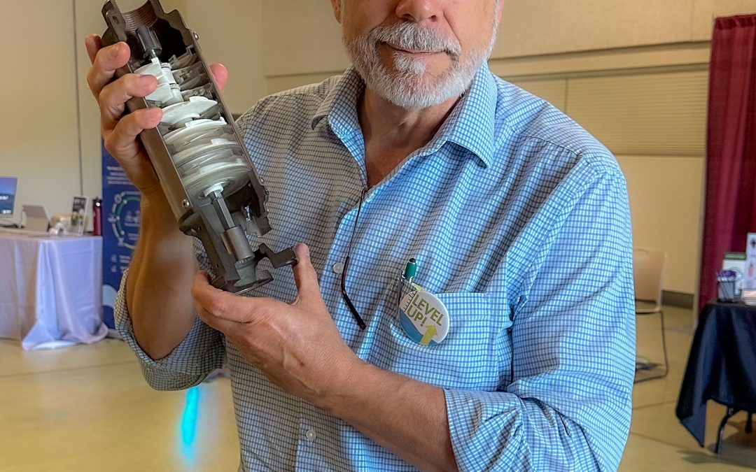 man in a blue shirt holds a mechanical part of a well